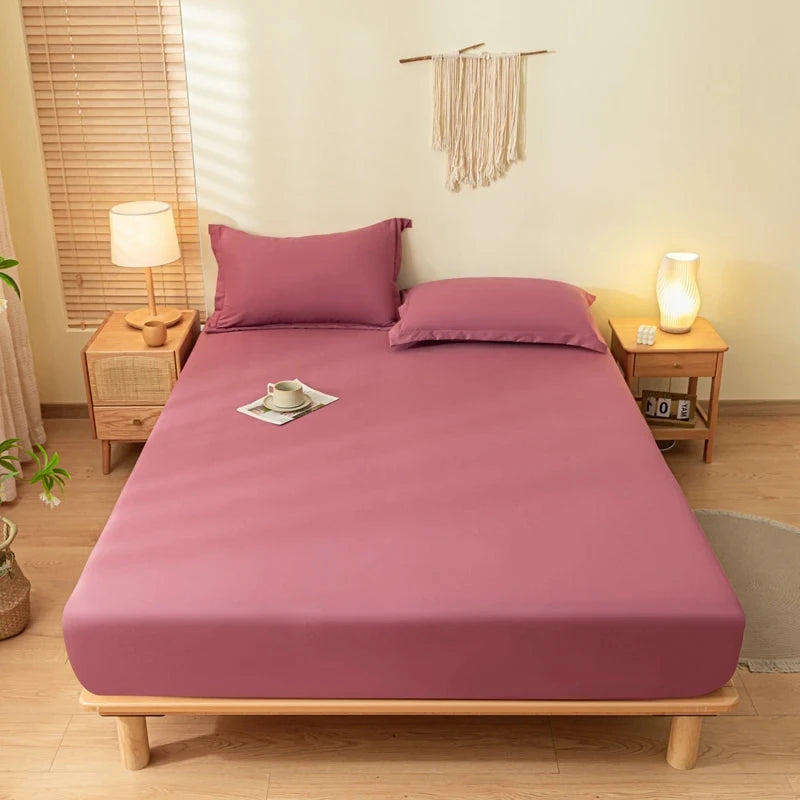 A pink fitted bed sheet set with matching pillowcases is displayed on a wooden bed frame in a bright bedroom.
