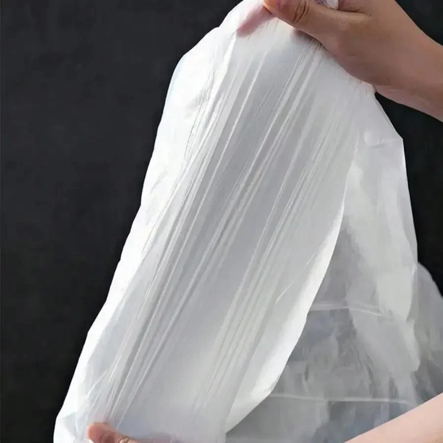 A hand is holding a large, clear plastic drawstring trash bag with handles against a dark background.