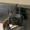 Black soft leather plaid crossbody bag with adjustable strap resting on a dark surface.