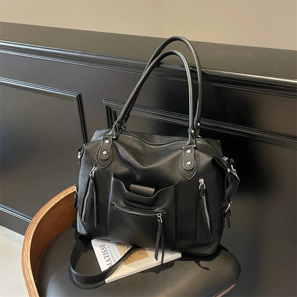 Black soft leather plaid crossbody bag with adjustable strap resting on a dark surface.