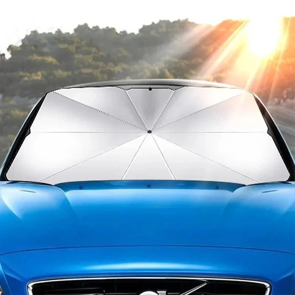 A silver foldable car windshield sunshade is installed on a blue car, with bright sunlight shining from the background.