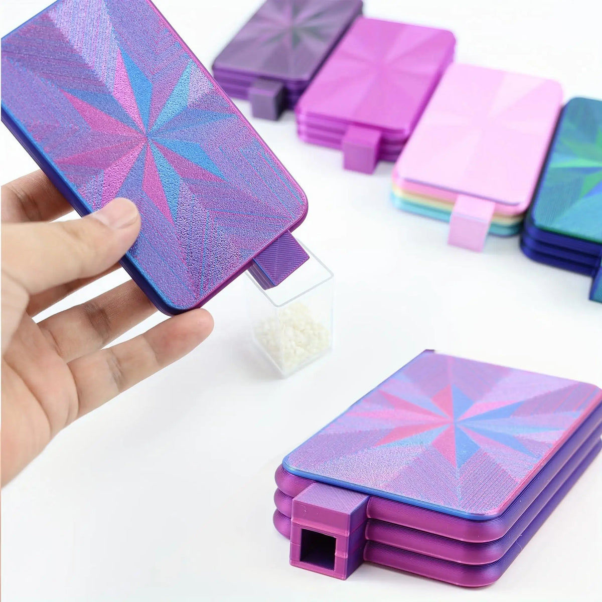 A hand holds a purple diamond painting pen set with steel tips and a tray of white beads.