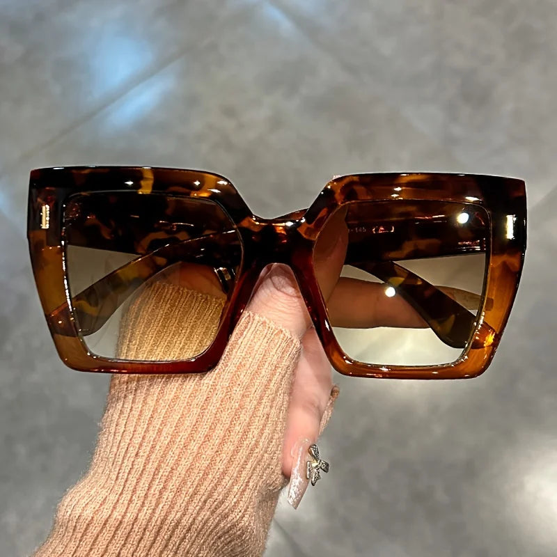 Brown tortoiseshell gradient square sunglasses being held by a person's hand