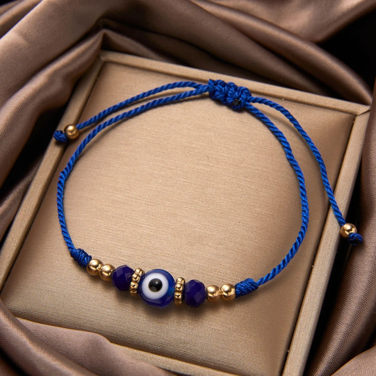 Blue thread bracelet with purple and white evil eye crystal beads on a beige box