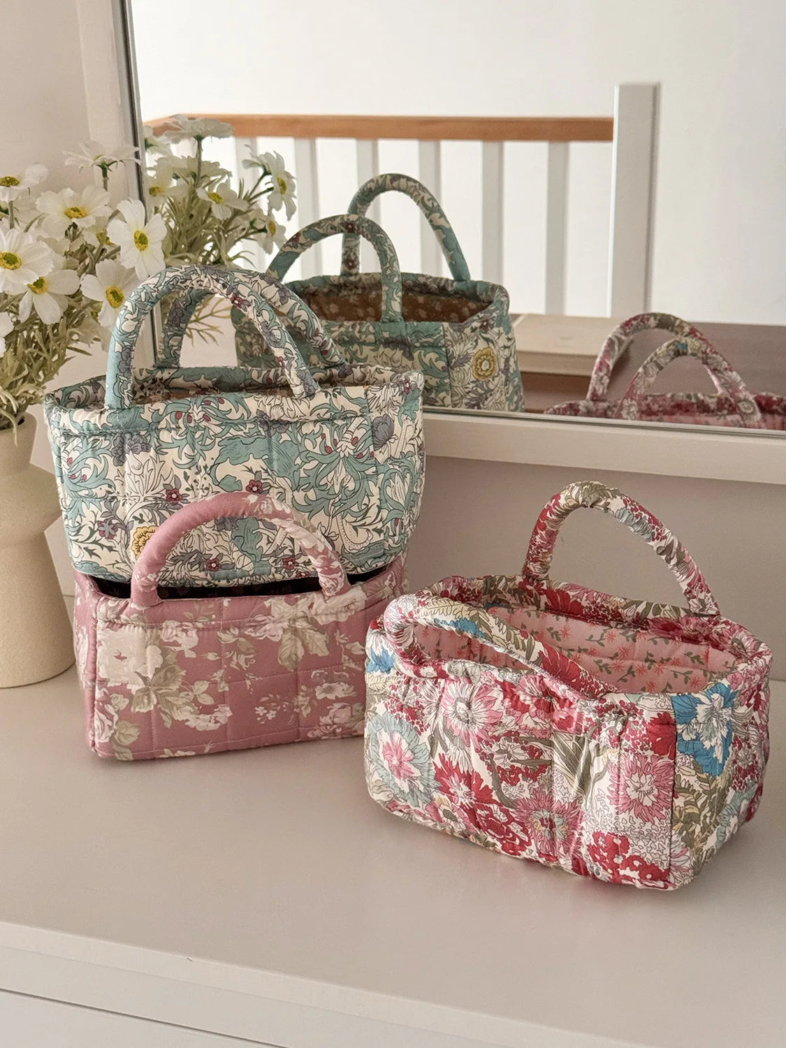 A collection of quilted fabric storage baskets in floral patterns and pinks displayed on a white shelf.