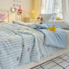 A light blue quilt with a playful cartoon print featuring small orange and white animals is displayed on a bed.
