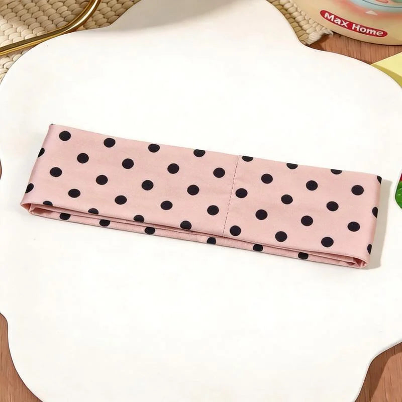 Un bandeau en tissu rose à pois noirs est exposé sur une surface blanche.