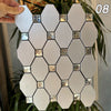 A hand holds a white mosaic wall tile panel featuring geometric shapes and silver accents.