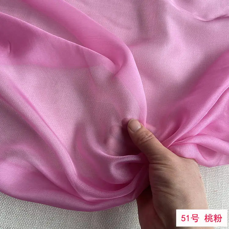 Close-up of pink mulberry silk chiffon fabric draped and being held by a hand.