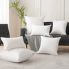 A collection of white square cushions and pillows displayed on a dark sofa with a striped throw blanket.
