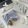A blue plaid floral embroidered makeup bag is shown next to a laptop and a white wireless mouse on a white desk.