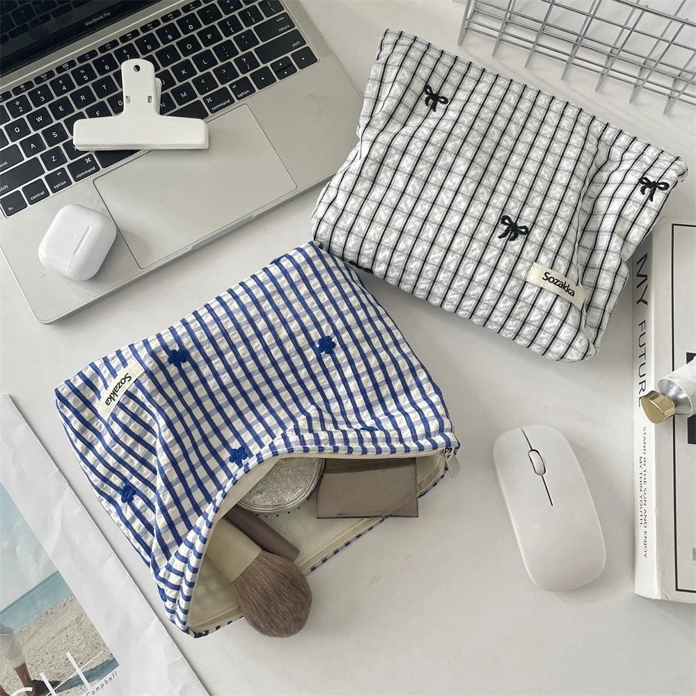 A blue plaid floral embroidered makeup bag is shown next to a laptop and a white wireless mouse on a white desk.