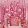A display of pink metallic foil balloons in various sizes hanging against a backdrop of pink drapery and floral accents.