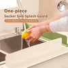 A hand is using a one-piece sucker sink splash guard to prevent splashing while washing fruit in a kitchen sink.