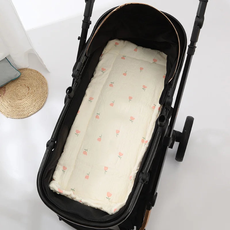 A black baby stroller seat cushion with a light cream fabric and pink floral embroidery is shown inside the carrier.
