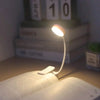 A white clip-on LED book light illuminates an open book on a wooden surface.