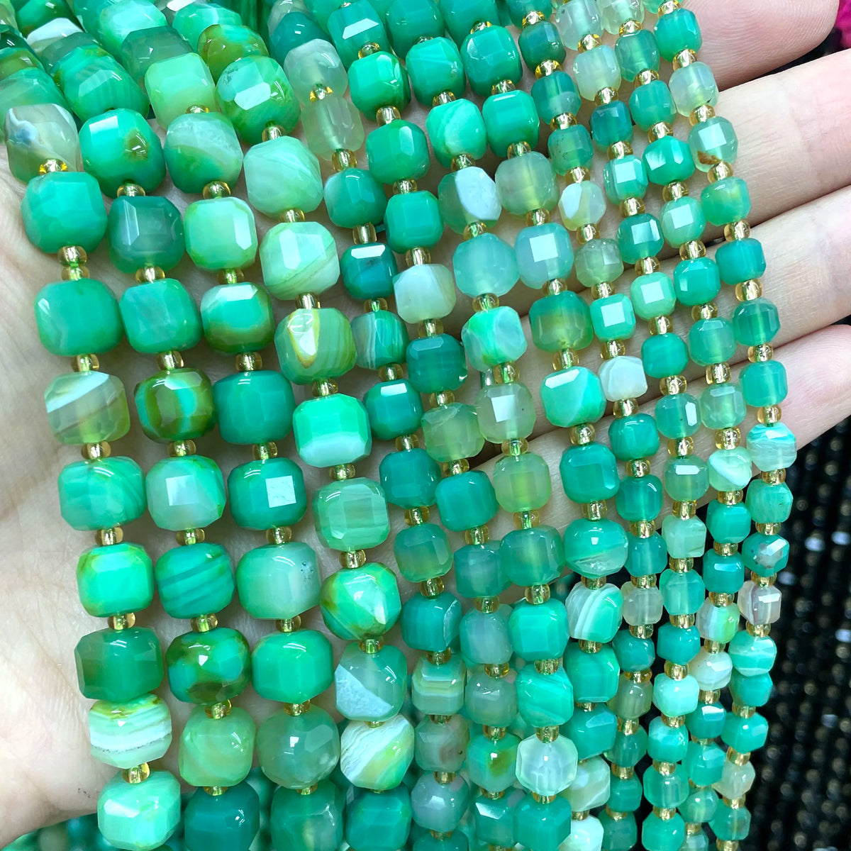 A close-up of green and aqua natural stone square faceted beads strung together for jewelry making