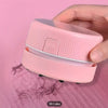 Eine Hand hält einen rosa Mini-Tischstaubsauger, der für das Säubern von Papier und Staub konzipiert ist.