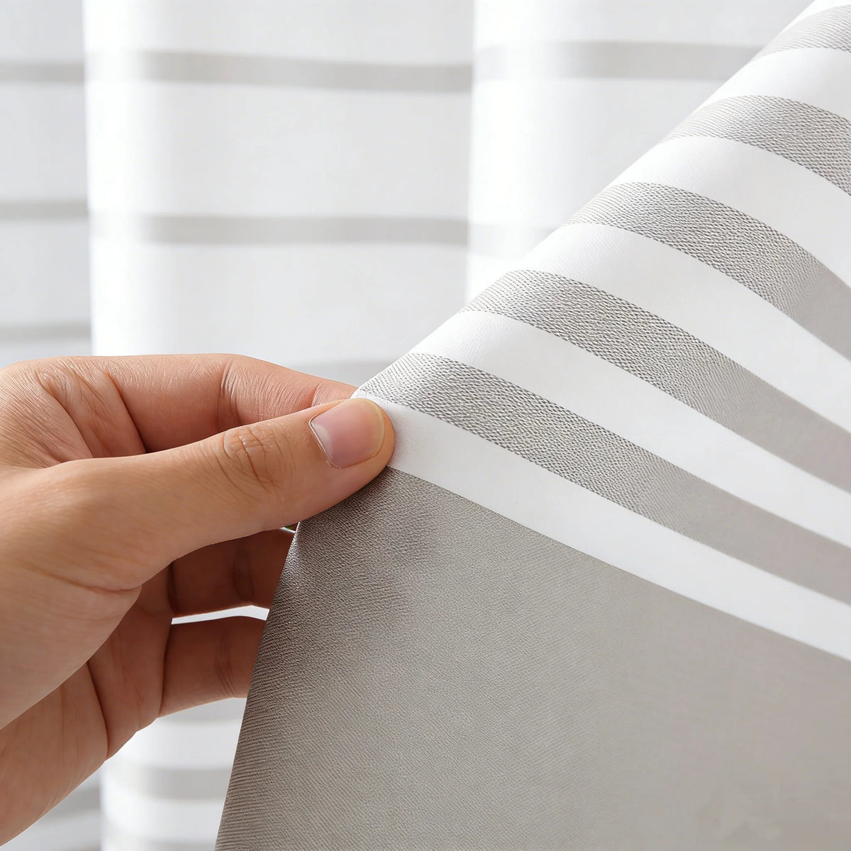 A hand is holding a modern striped shower curtain fabric with embossed texture, showing gray and white stripes.