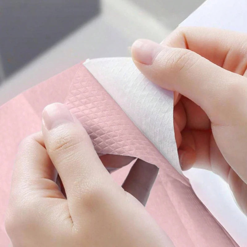 A hand is holding a white disposable toilet seat cover over a pink paper product.