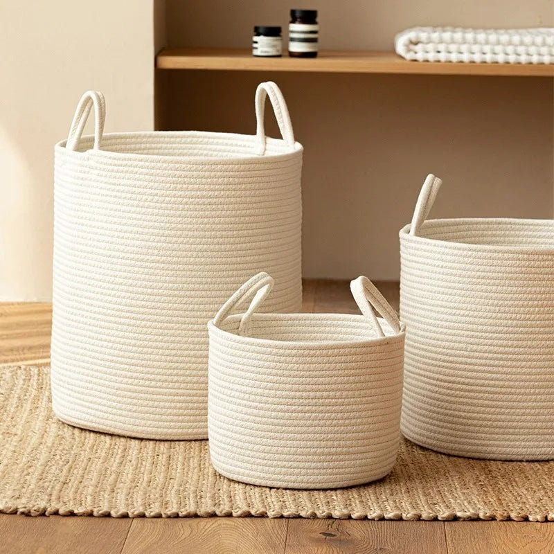 A white handwoven cotton rope storage basket with handles sitting on a woven mat.