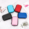 A collection of colorful portable electronics organizer pouches in black, blue, red, and pink resting on a white marble surfa