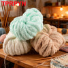 A pile of light green and beige chunky chenille yarn for knitting and crochet displayed on a wooden surface.