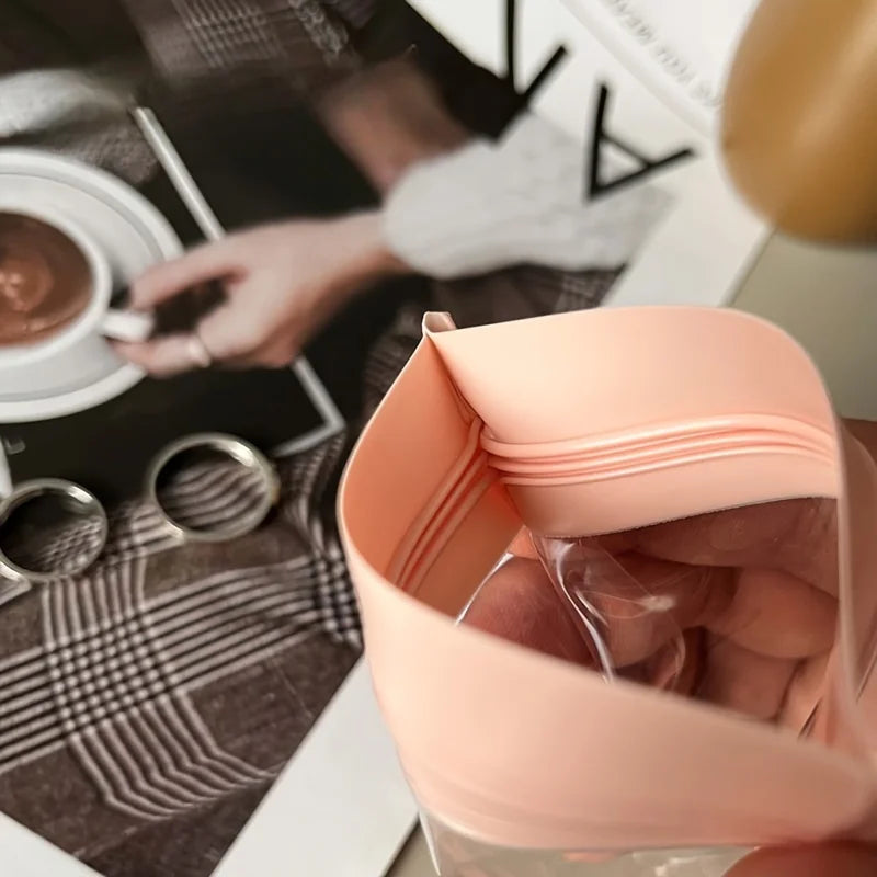 A hand holds a pink self-sealing jewelry storage bag, showcasing the clear pouch inside.