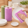 A hand is using a purple reusable tear-away cleaning cloth on a white plate, with rolls of the same cloth nearby.