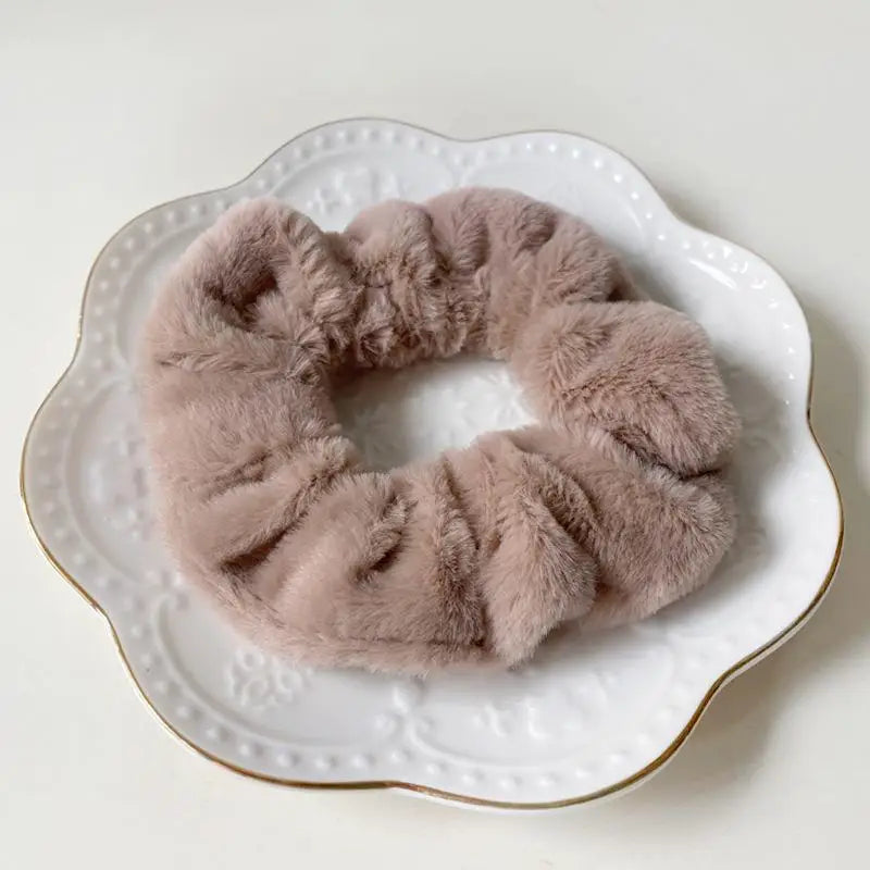 A round, fluffy, light pink coil hair tie resting on a white plate.