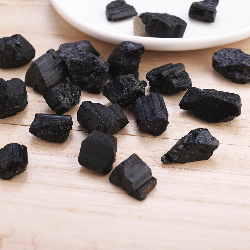 A collection of raw black tourmaline specimens scattered on a light wooden surface with a white plate in the background.