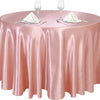 A round table set with a pink satin tablecloth, glassware, and silverware for an event.