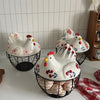 A rustic ceramic hen-shaped egg basket with a lid, featuring white and pink painted chickens.