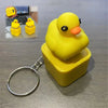 A yellow rubber duck fidget keychain with sound and LED lights resting in a yellow plastic container.