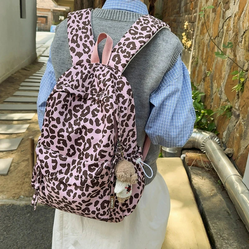 A person is wearing a leopard print nylon backpack with multiple pockets over a gray sweater and blue shirt.