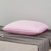 A pink luxury goose down and feather pillow with a cotton cover resting on a gray fabric.