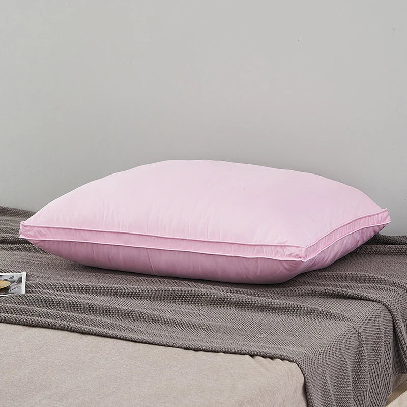 A pink luxury goose down and feather pillow with a cotton cover resting on a gray fabric.