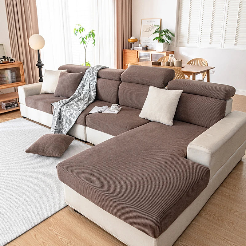 Sofá modular moderno en tela marrón y crema con manta y cojines grises, ubicado en una sala de estar luminosa.