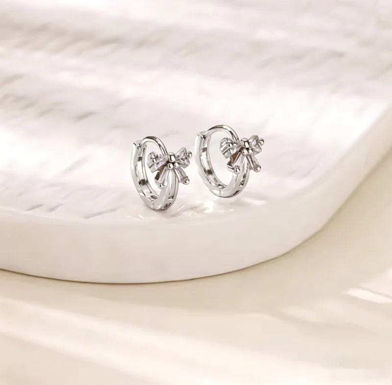 Pendientes de aro plateados con detalles florales sobre una superficie blanca.