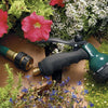 A green garden hose quick connector set is shown next to red and pink flowers in a garden setting.