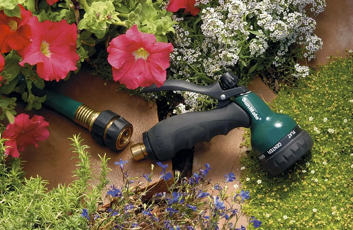 A green garden hose quick connector set is shown next to red and pink flowers in a garden setting.