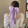 A woman with dark hair wearing a white blouse and a purple silk bow tied in her hair.