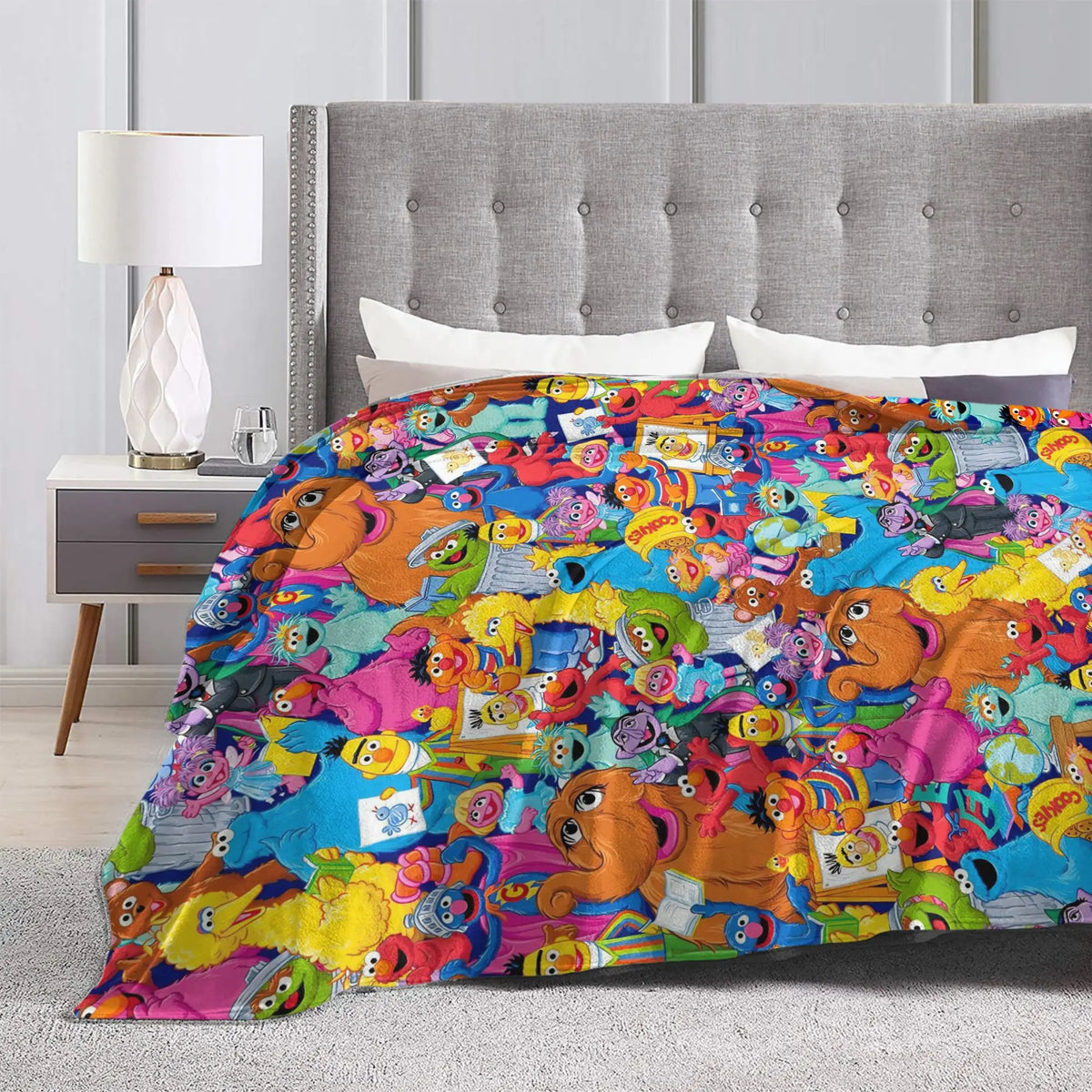 A colorful flannel throw blanket featuring characters from Sesame Street and Friends draped over a bed.