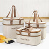 A beige insulated lunch bag with brown straps and thermal lining is shown on a white surface.