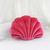 A vibrant pink velvet shell shaped throw pillow resting on white bedding.