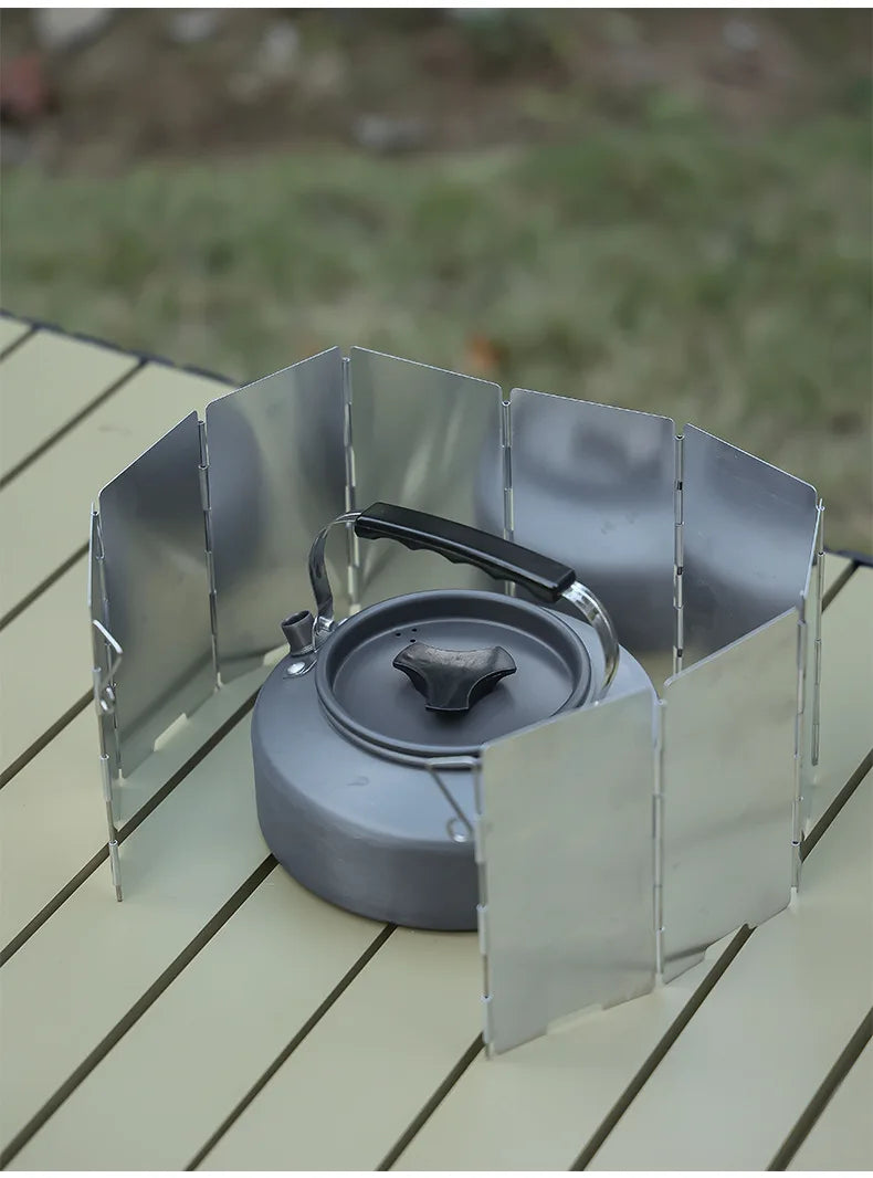 A portable aluminum alloy windshield designed for camping stoves, shown resting on a wooden surface.