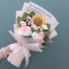 Handgemachter Häkelblumenstrauß mit rosa und weißen Blumen und grünem Laub, in rosa Papier eingewickelt.