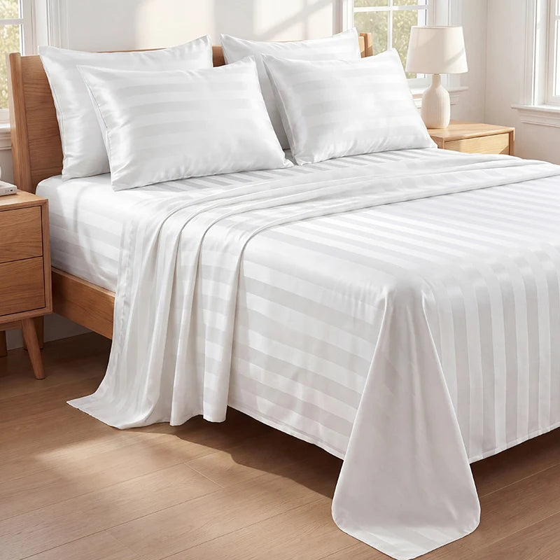 White and light gray striped satin bedding set on a wooden bed with pillows and a draped sheet.