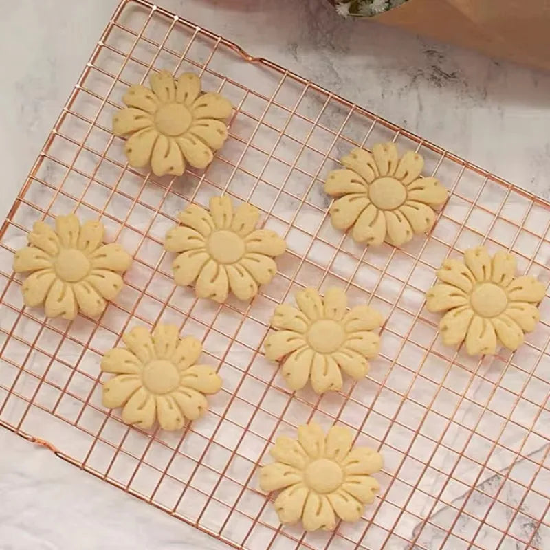 A set of floral cookie cutters in peach, cherry blossom, and sunflower designs arranged on a wire rack.