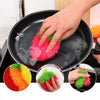 A hand is using a pink strawberry scrubber sponge to clean a black frying pan.